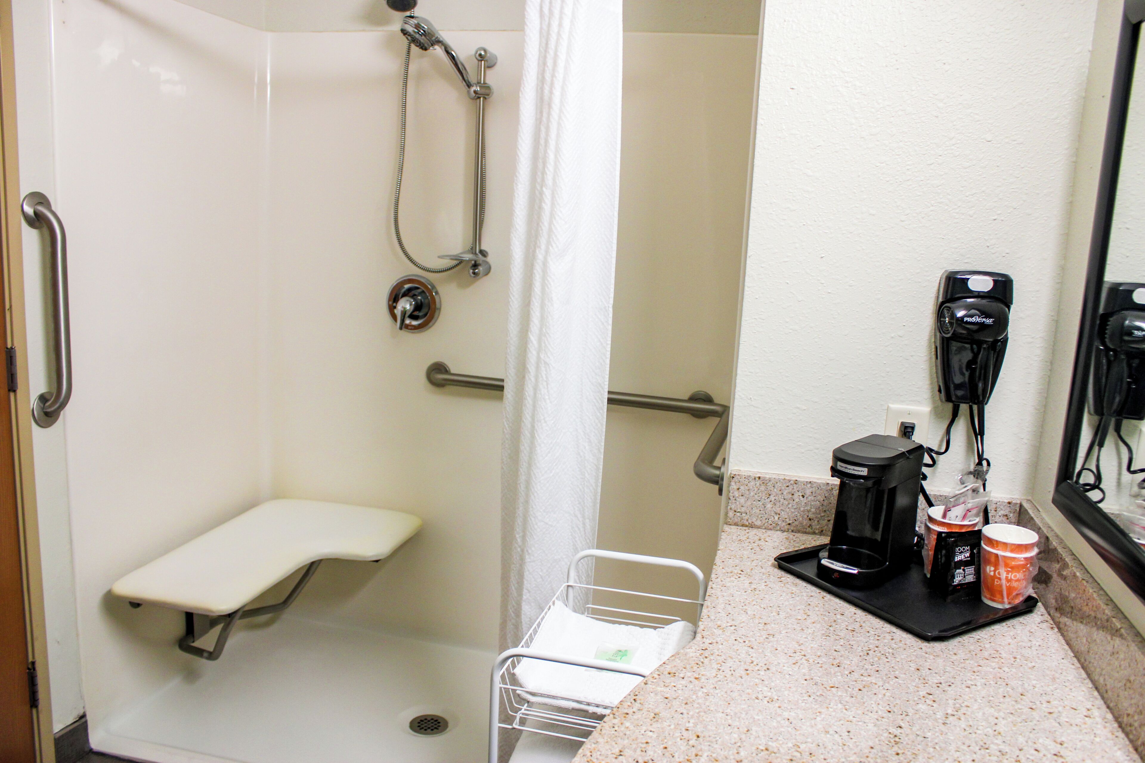 A bathroom with a shower, a toilet, a sink, a coffee maker, and a cup of coffee.