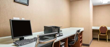 A hotel room with a desk, computer, and chairs.