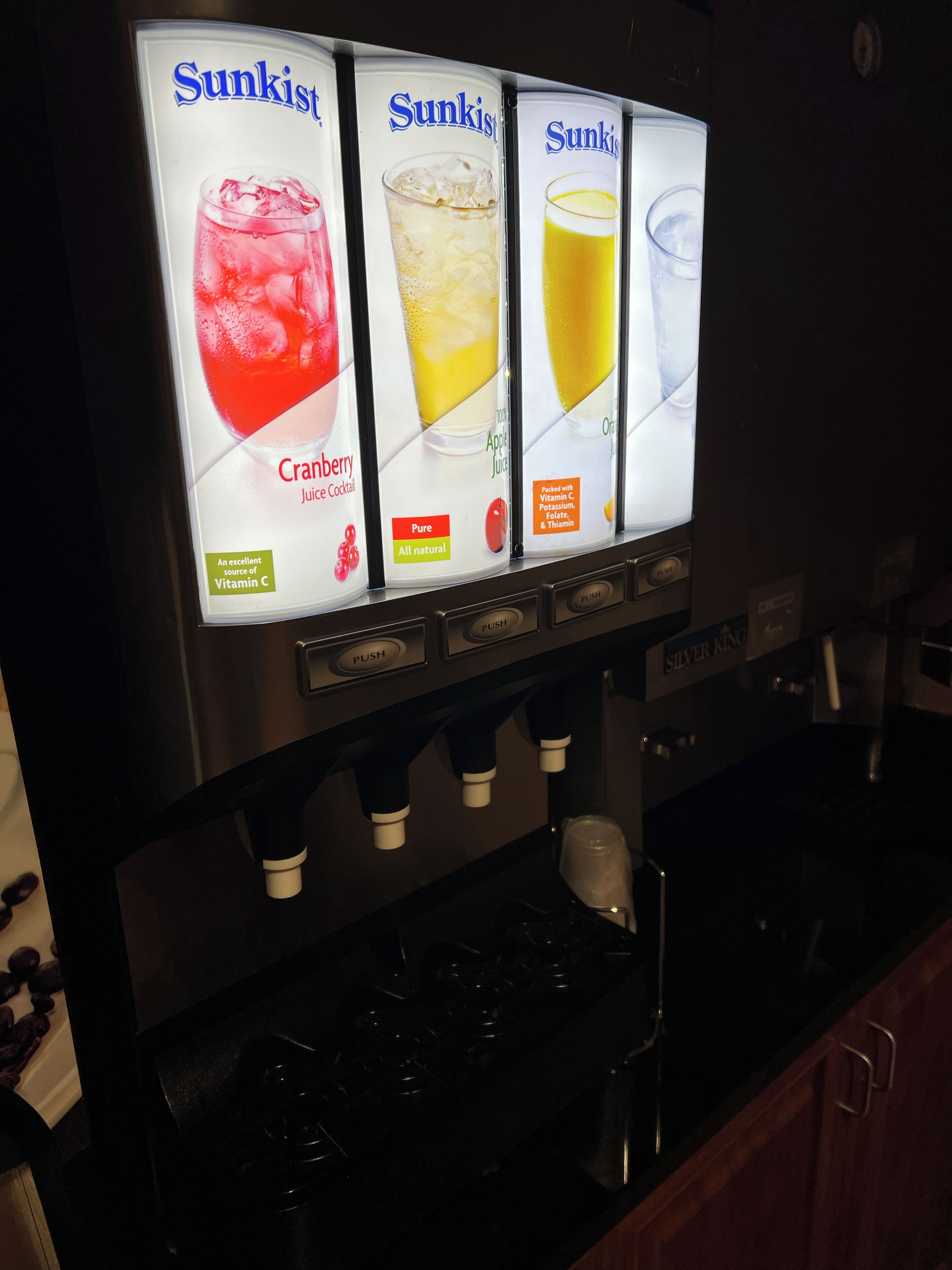 Dispensador de bebidas con tres opciones: cóctel de jugo de arándano, jugo de manzana y jugo de naranja.