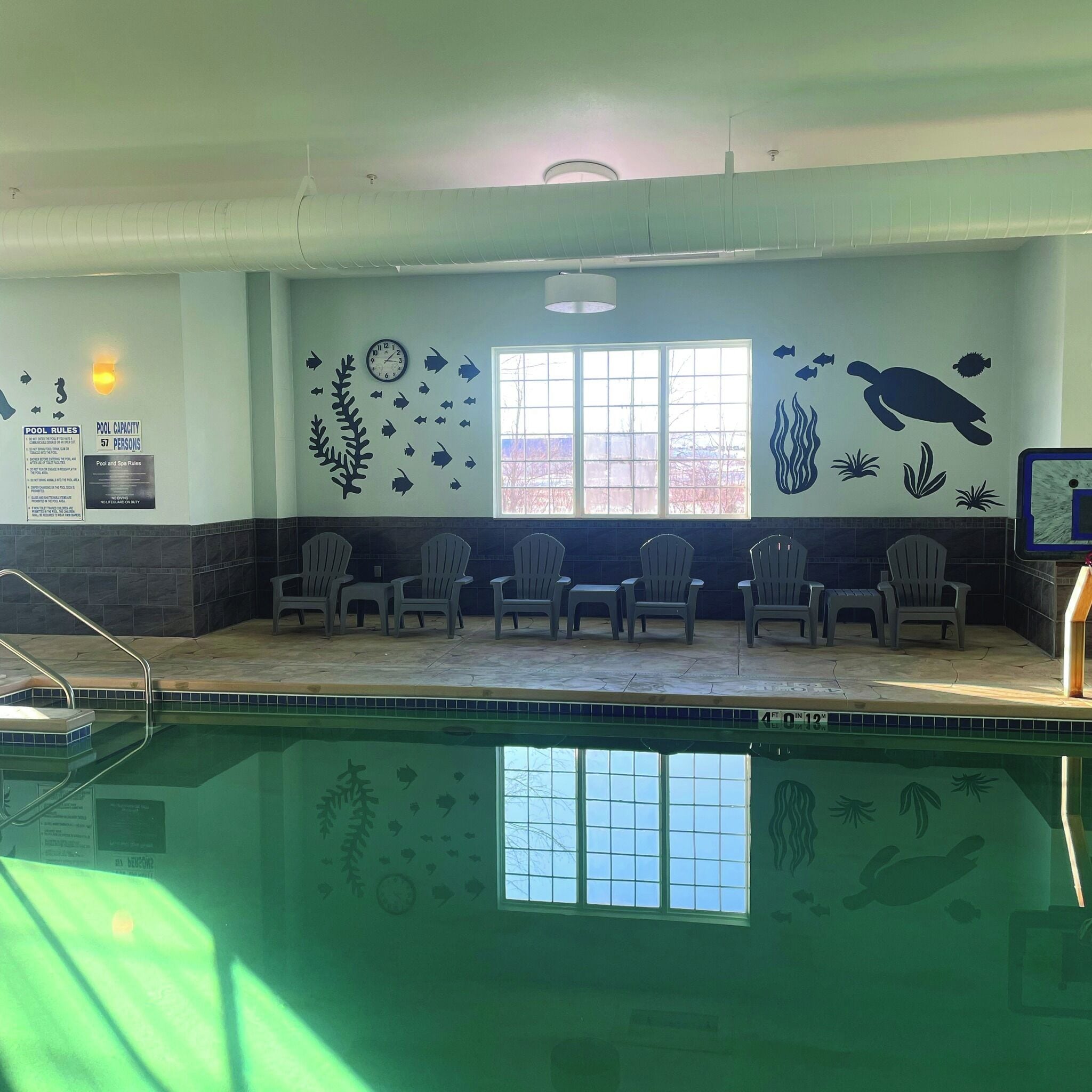 Uma área de piscina com cadeiras, um relógio e decorações de parede com tema aquático.
