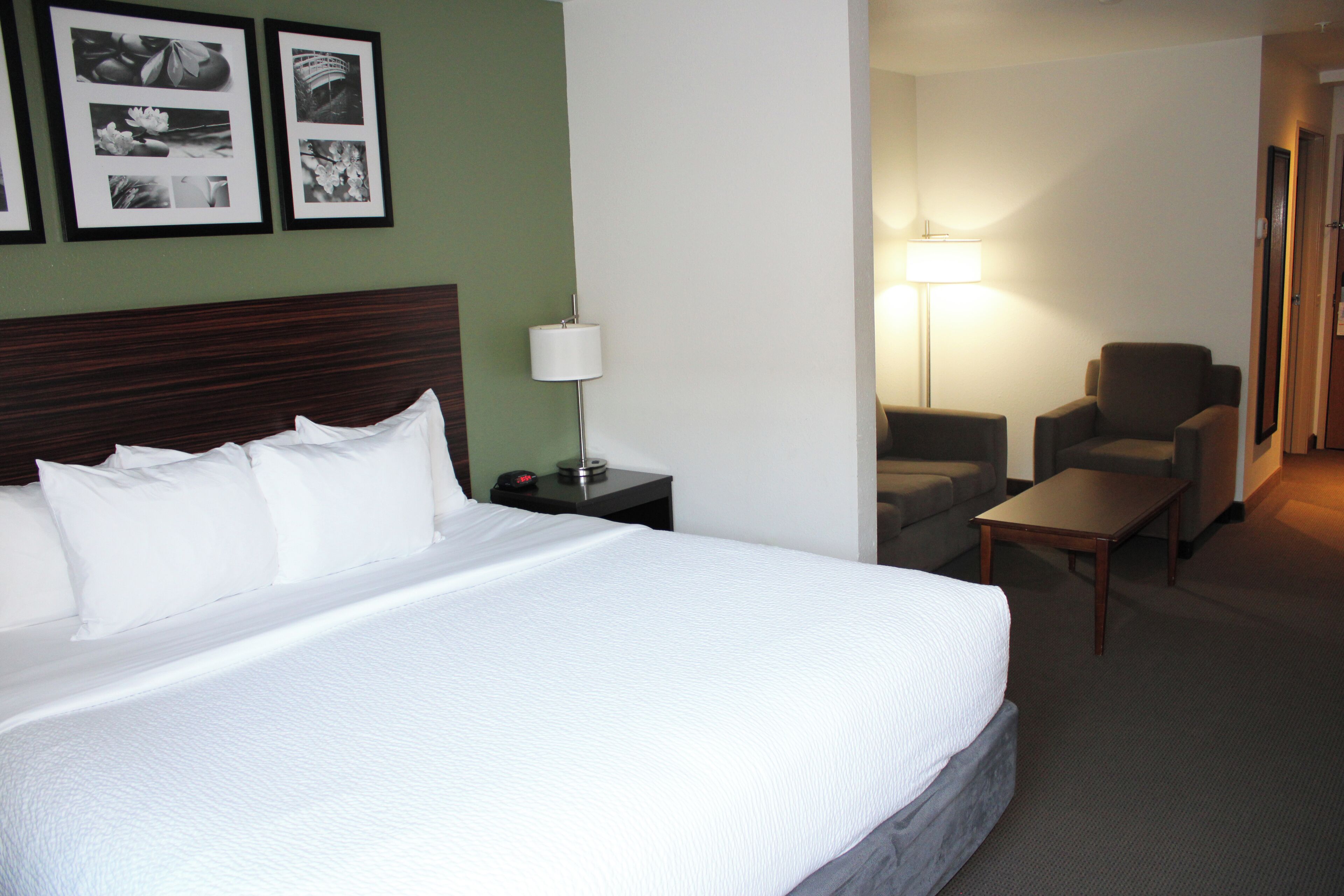 Habitación de hotel con una cama grande, una mesita de noche con lámpara, una silla y una pequeña mesa.