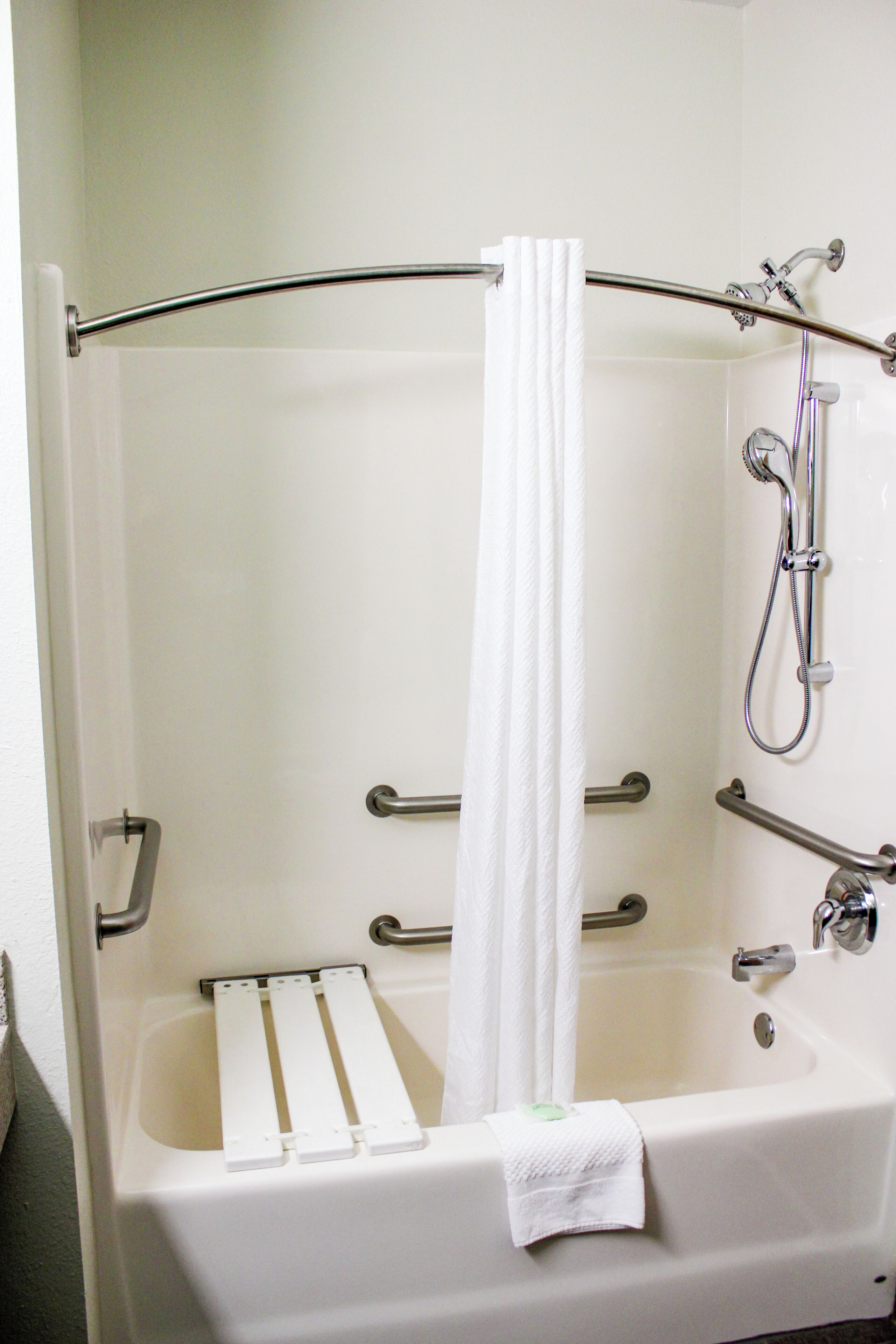 A white bathtub with a shower head, grab bars, and a towel.