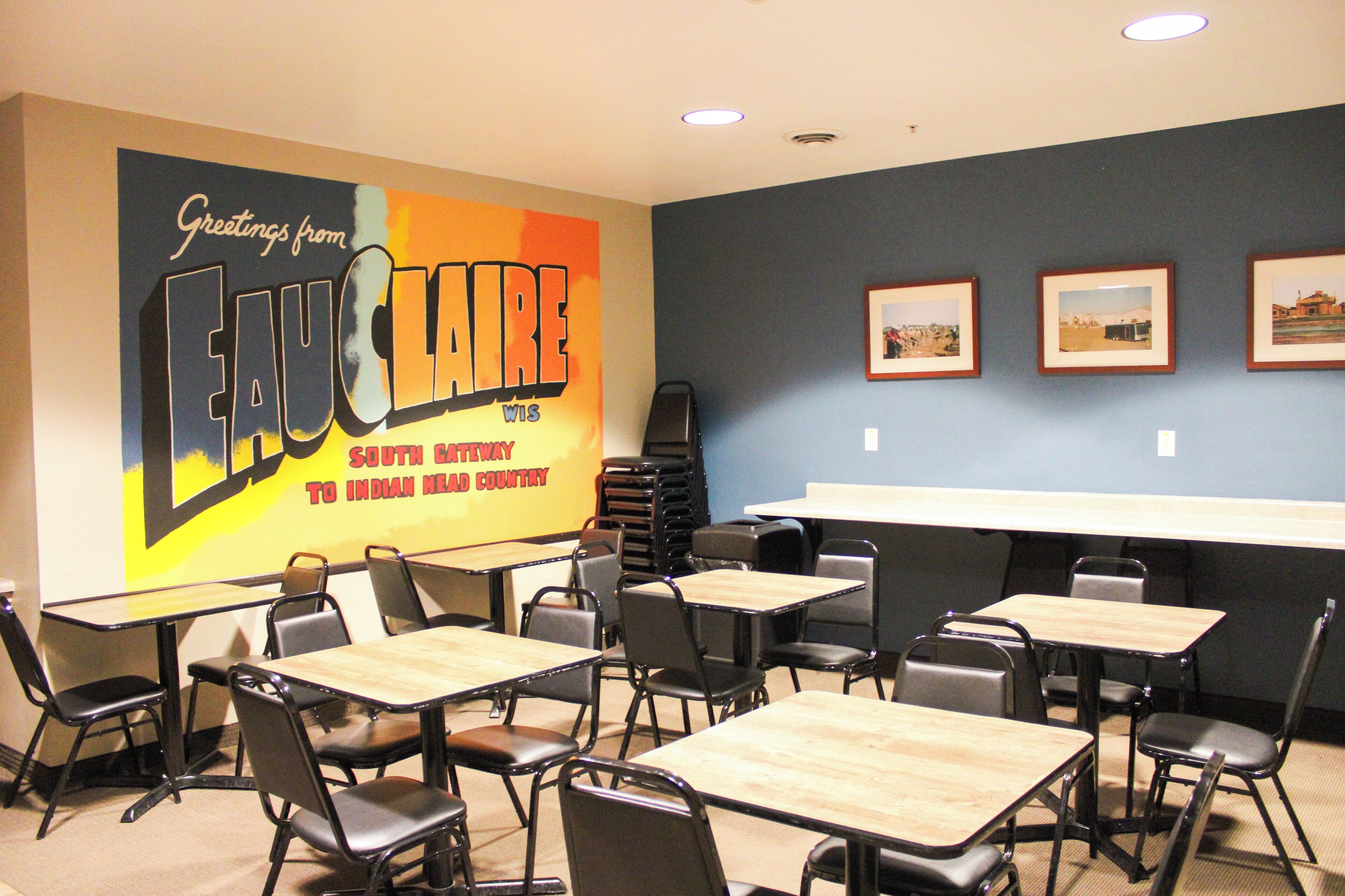 A conference room with tables and chairs, a large poster on the wall, and framed pictures on the wall.