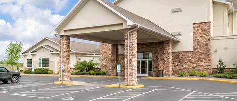 A hotel entrance with a covered parking area, handicap accessible spaces, and a stone facade.