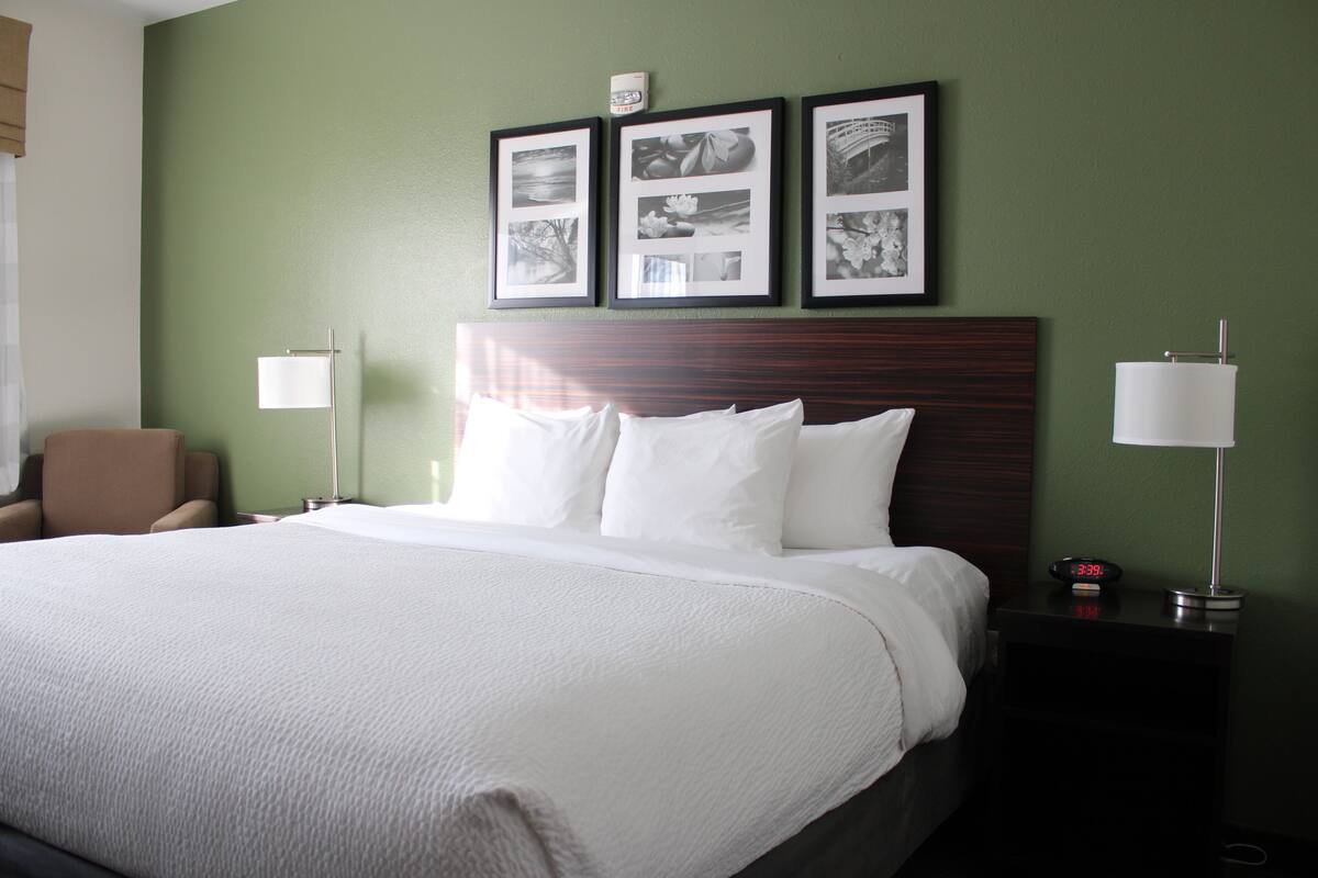 A hotel room with a large bed, a chair, a nightstand with a lamp, and framed pictures on the wall.