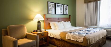 A hotel room with a bed, a chair, a nightstand with a lamp, and framed pictures on the wall.