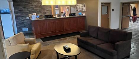 A hotel lobby with a reception desk, a chandelier, sofas, and a coffee table.