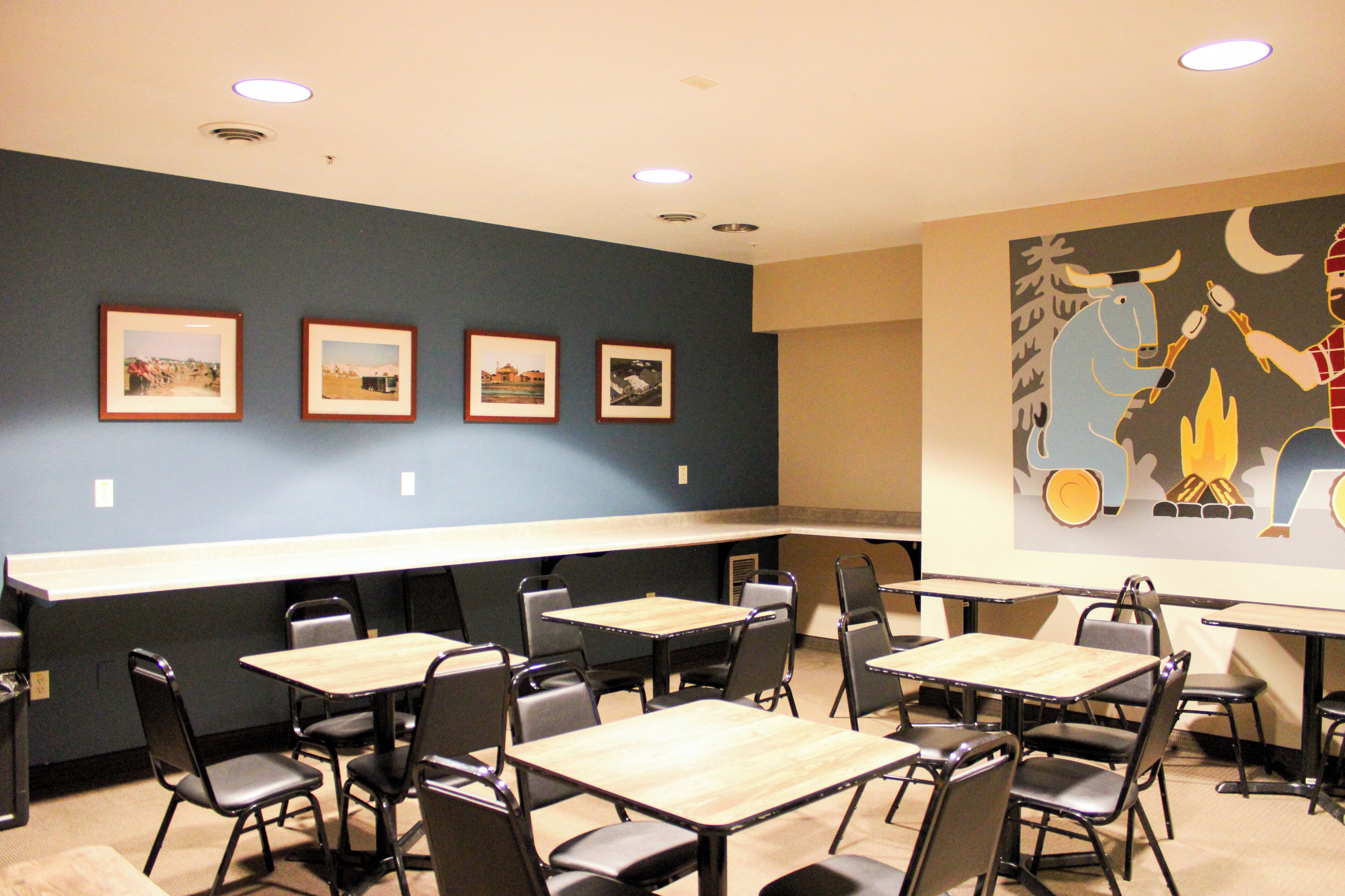 A conference room with tables and chairs, framed pictures on the wall, and a mural.