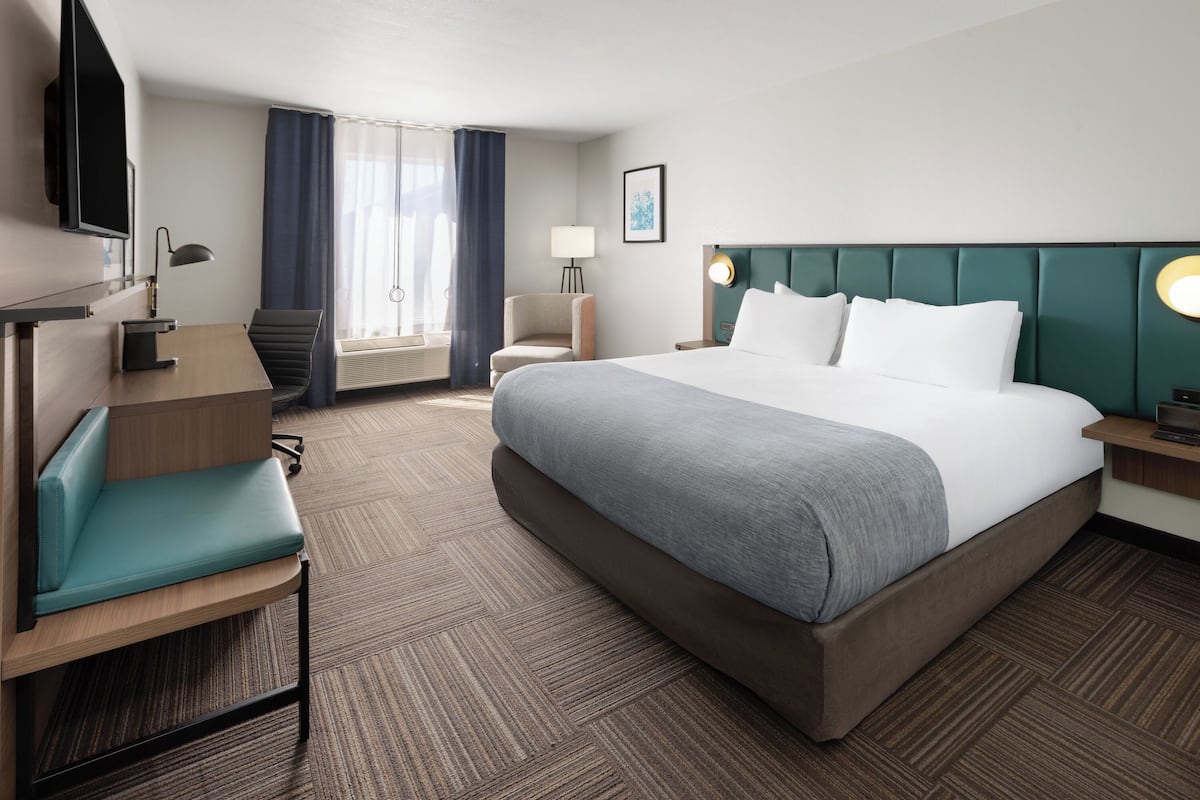 Ein Hotelzimmer mit einem großen Bett, einem Schreibtisch, einem Sessel, einem Fernseher und einem Fenster mit Vorhängen.