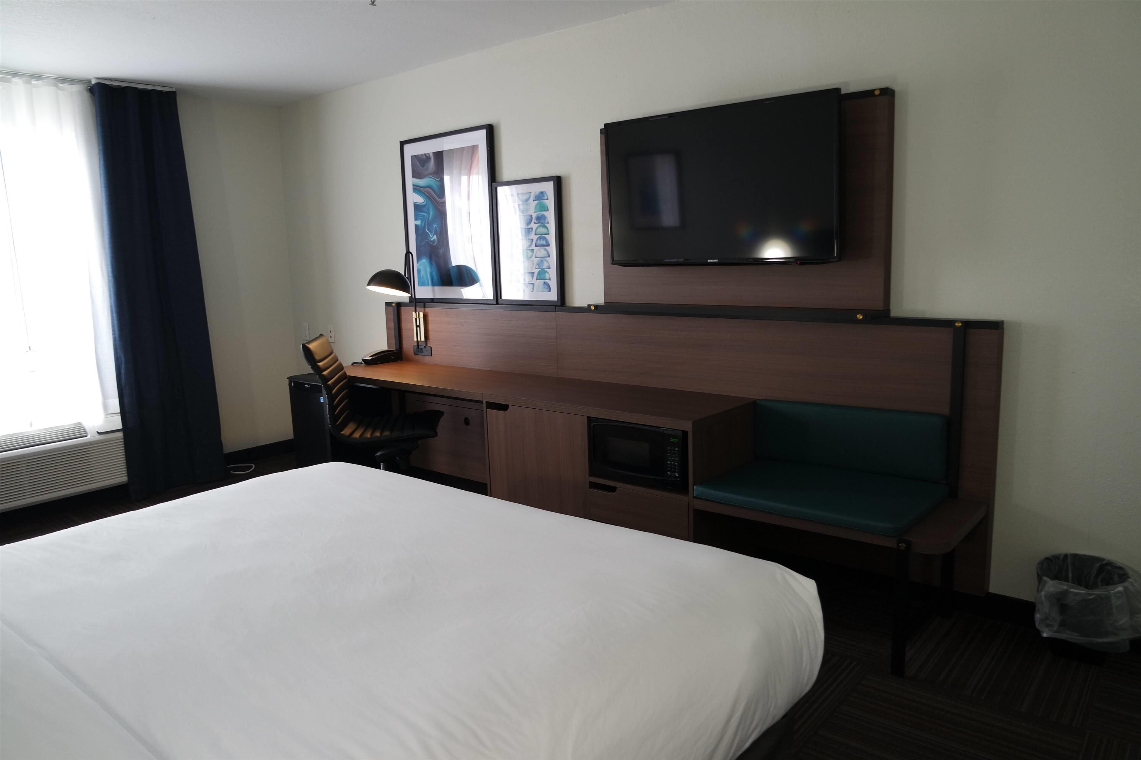 A hotel room with a bed, a desk with a chair, a television, and a microwave.
