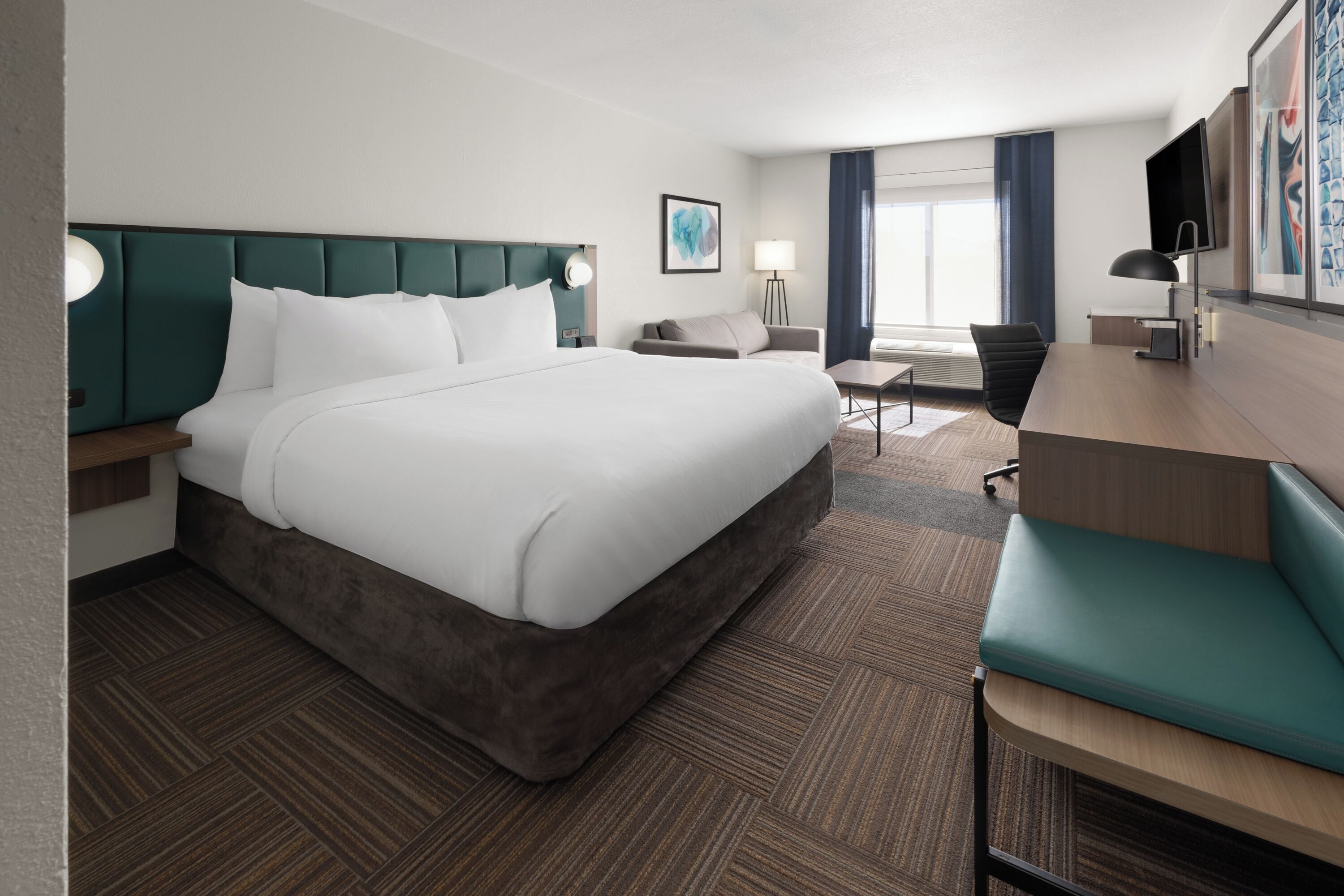 Habitación de hotel con una cama grande, un escritorio, una silla, un televisor y una ventana con cortinas.