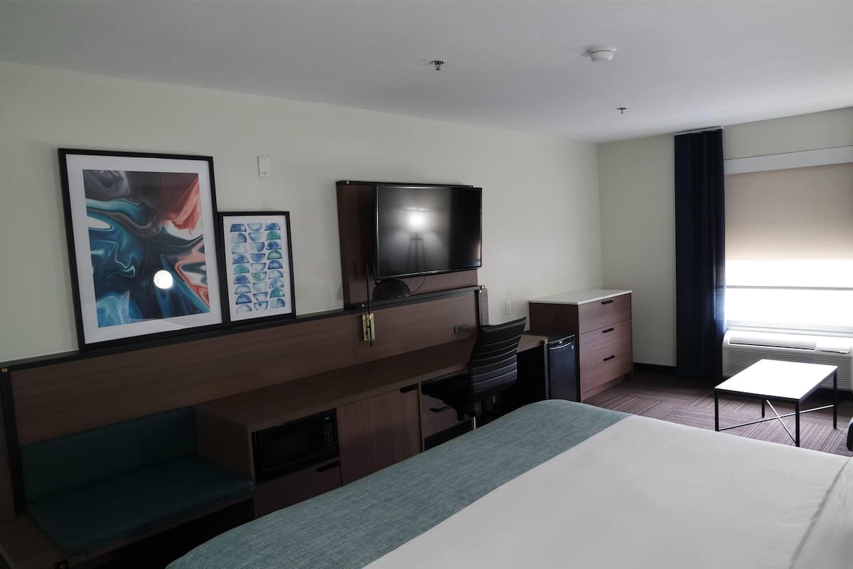 Ein Hotelzimmer mit Bett, Schreibtisch, Stuhl, Fernseher und Bildern an der Wand.