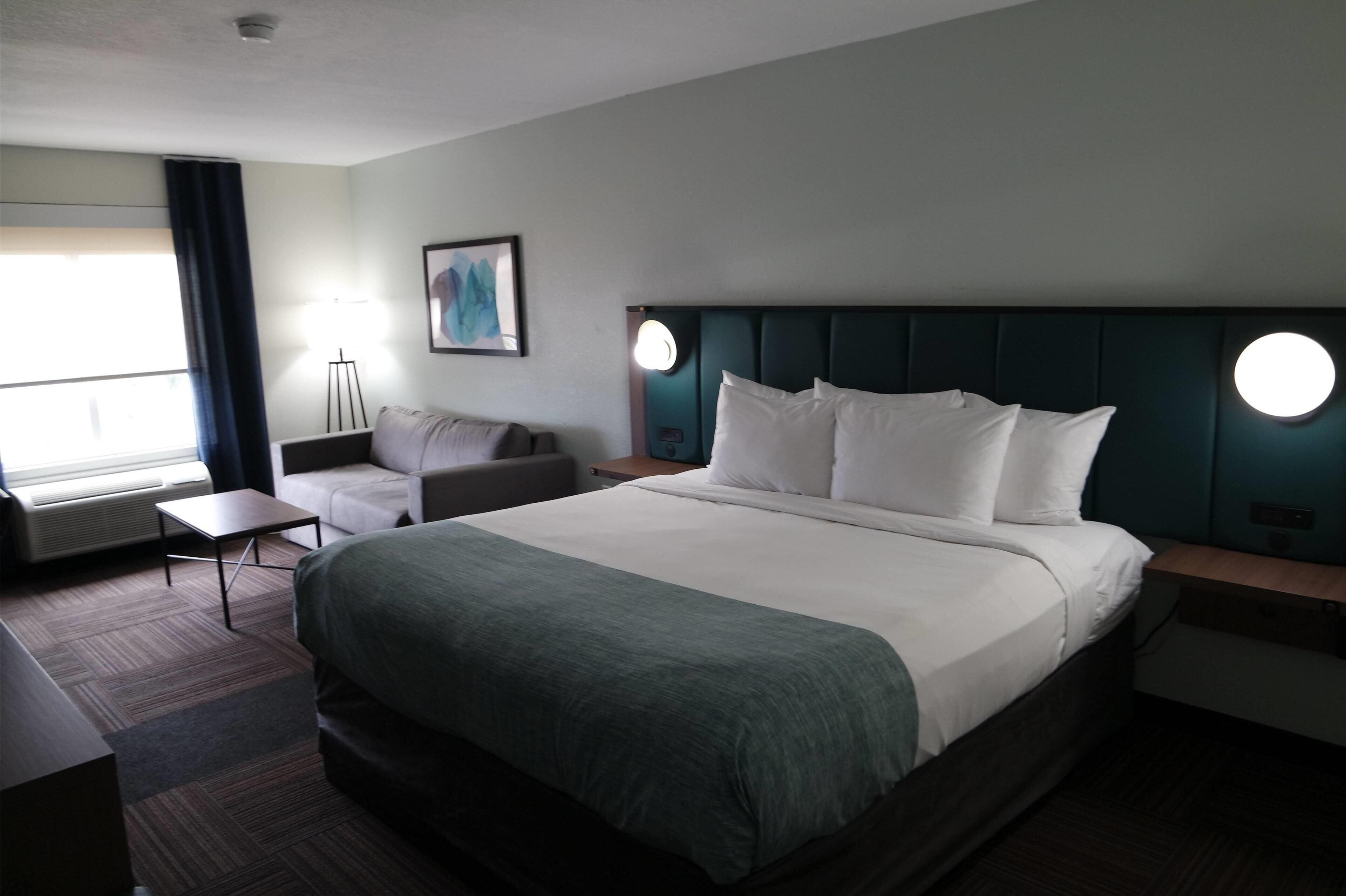 A hotel room with a large bed, a desk, a chair, a sofa, and a window with curtains.