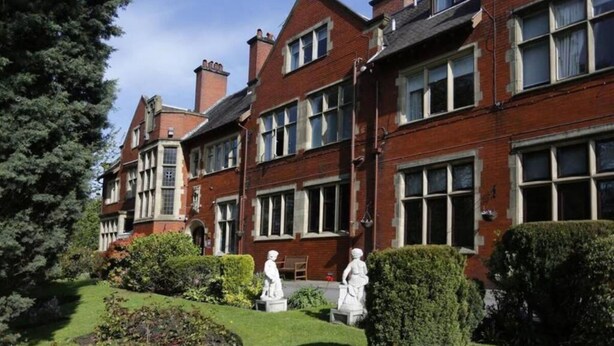 Un edificio tradicional de ladrillo rojo con múltiples ventanas y un jardín bien cuidado con estatuas.