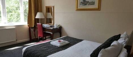 A hotel room with a bed, a desk, a chair, a lamp, and a window with curtains.