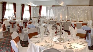 Un salón de banquetes con mesas redondas dispuestas para un evento formal, decorado con manteles blancos y cubertería de plata.