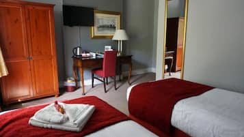 A hotel room with two beds, a desk with a chair, a wardrobe, a painting on the wall, and a mirror.