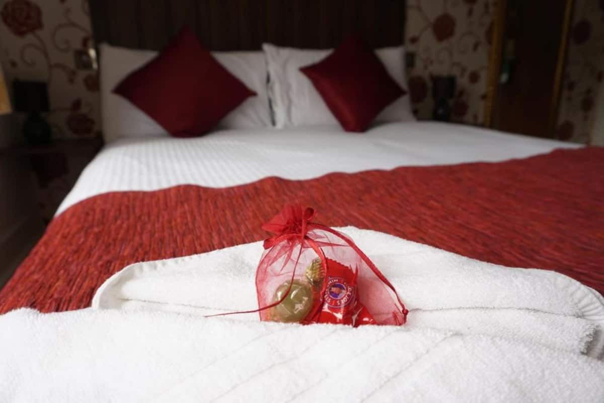 Un letto con una coperta rossa e cuscini, un piumone bianco e una piccola confezione regalo sopra il letto.