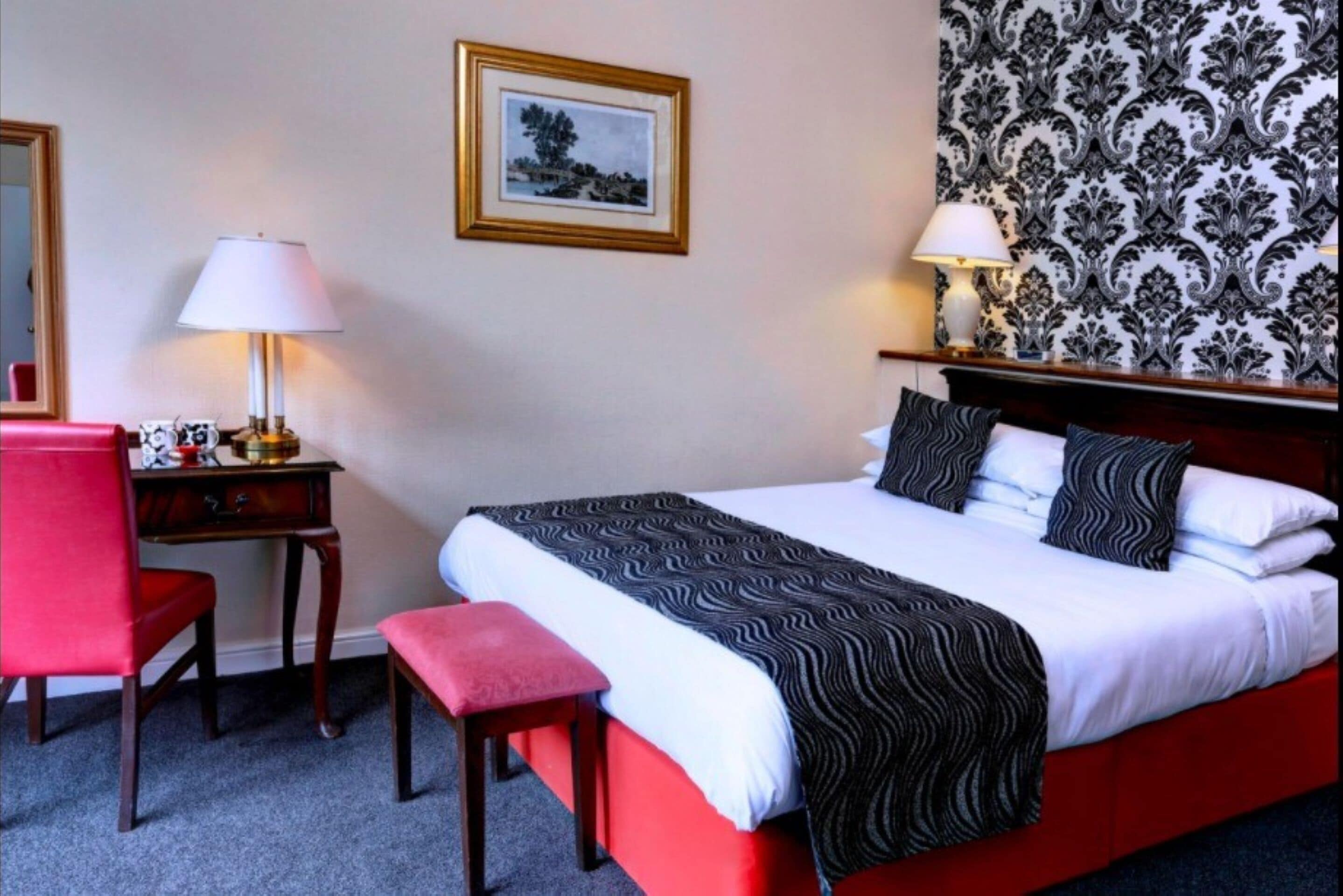 Et hotelværelse med seng, skrivebord, stol, bænk og to lamper.