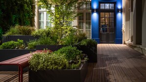 A wooden deck with planters and a bench, leading to a dark blue door with glass panels. - Residence & Spa Le Prince Regent (Paris)