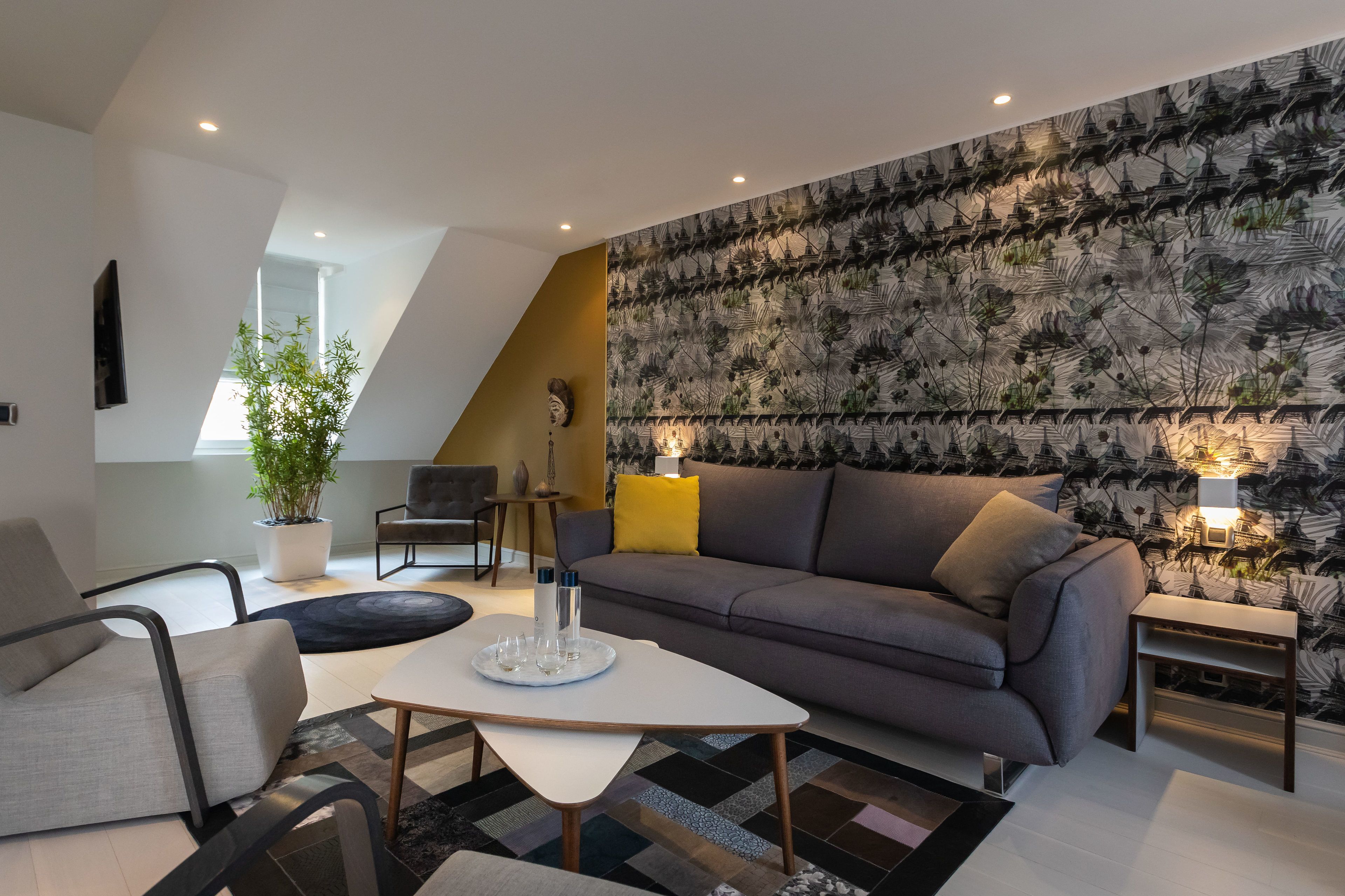 A modern living room with a grey sofa, a white coffee table, and a patterned wallpaper.