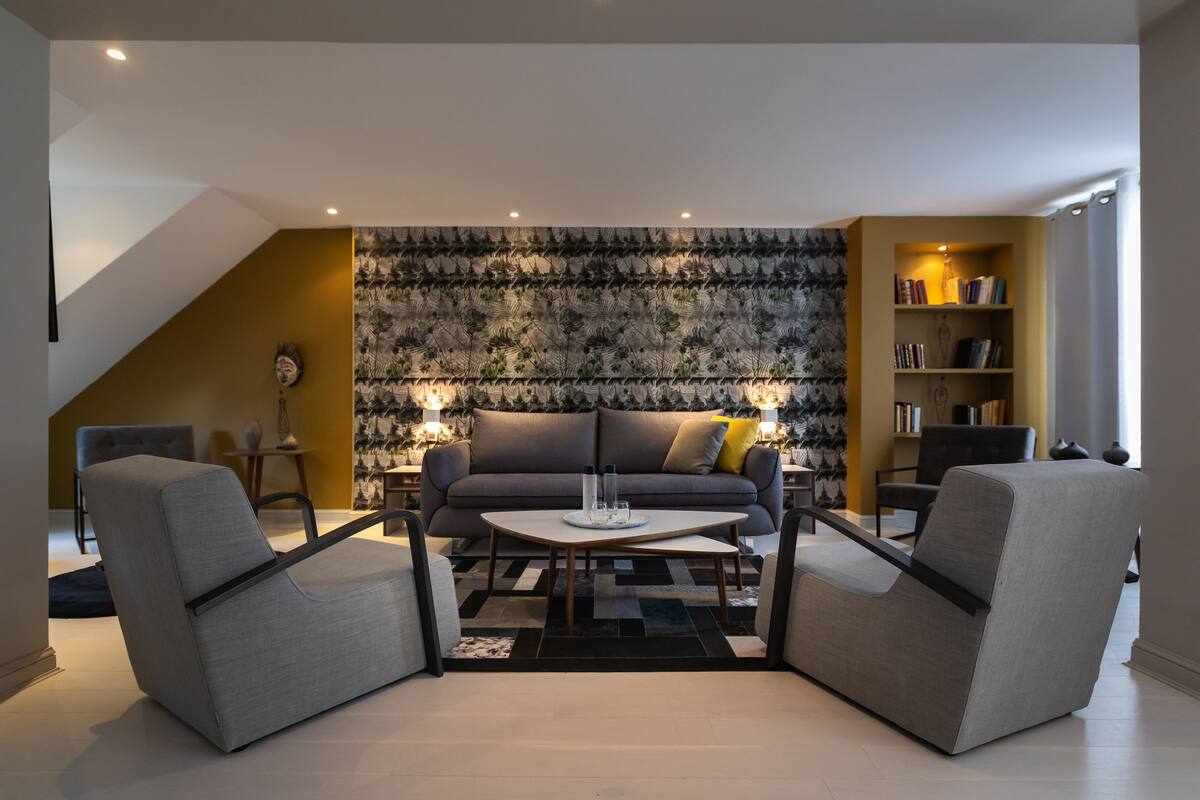 A modern living room with a sofa, two armchairs, a coffee table, and a bookshelf.