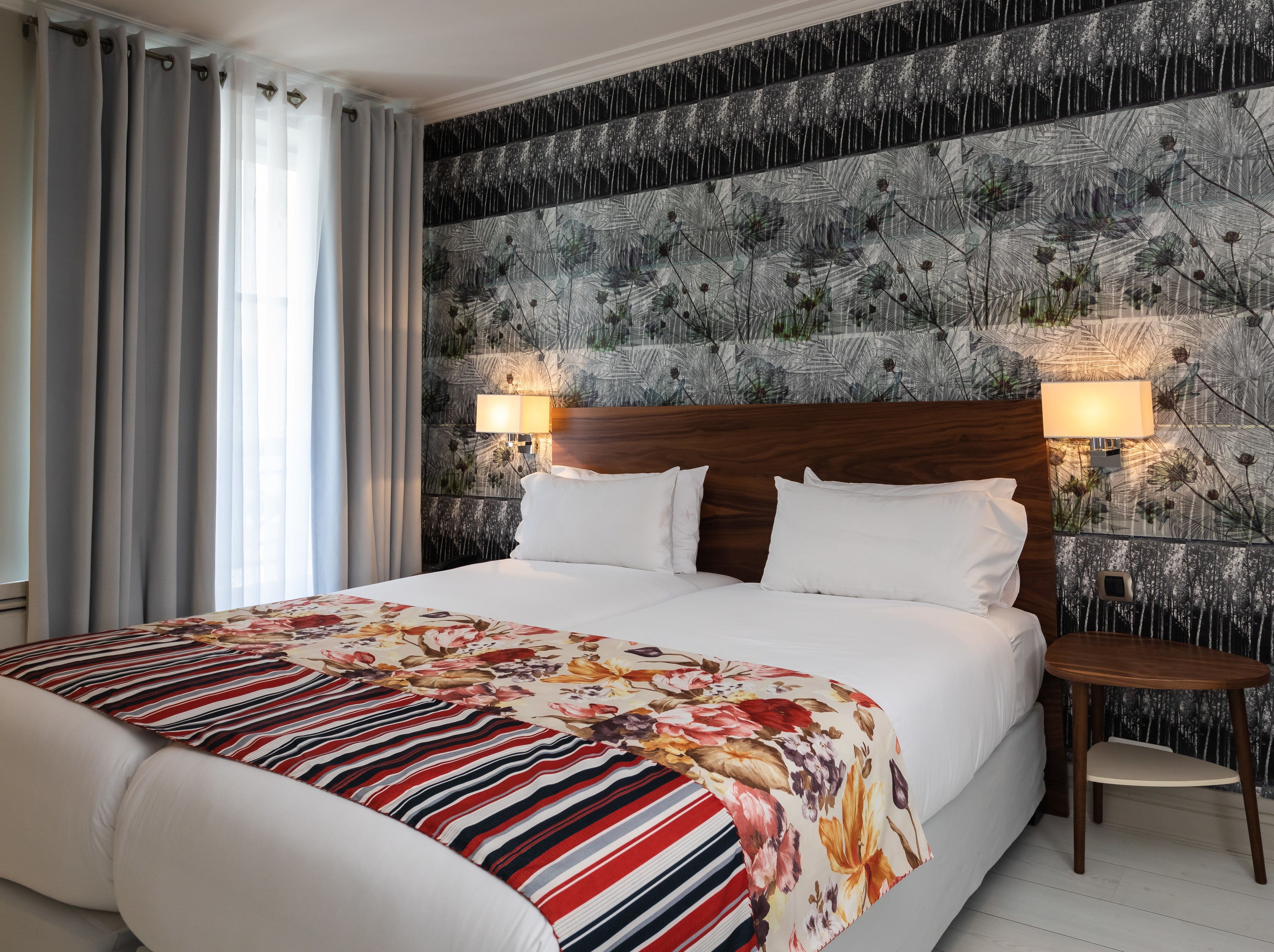 A hotel room with a large bed, two bedside lamps, a small wooden side table, and a floral-patterned headboard.