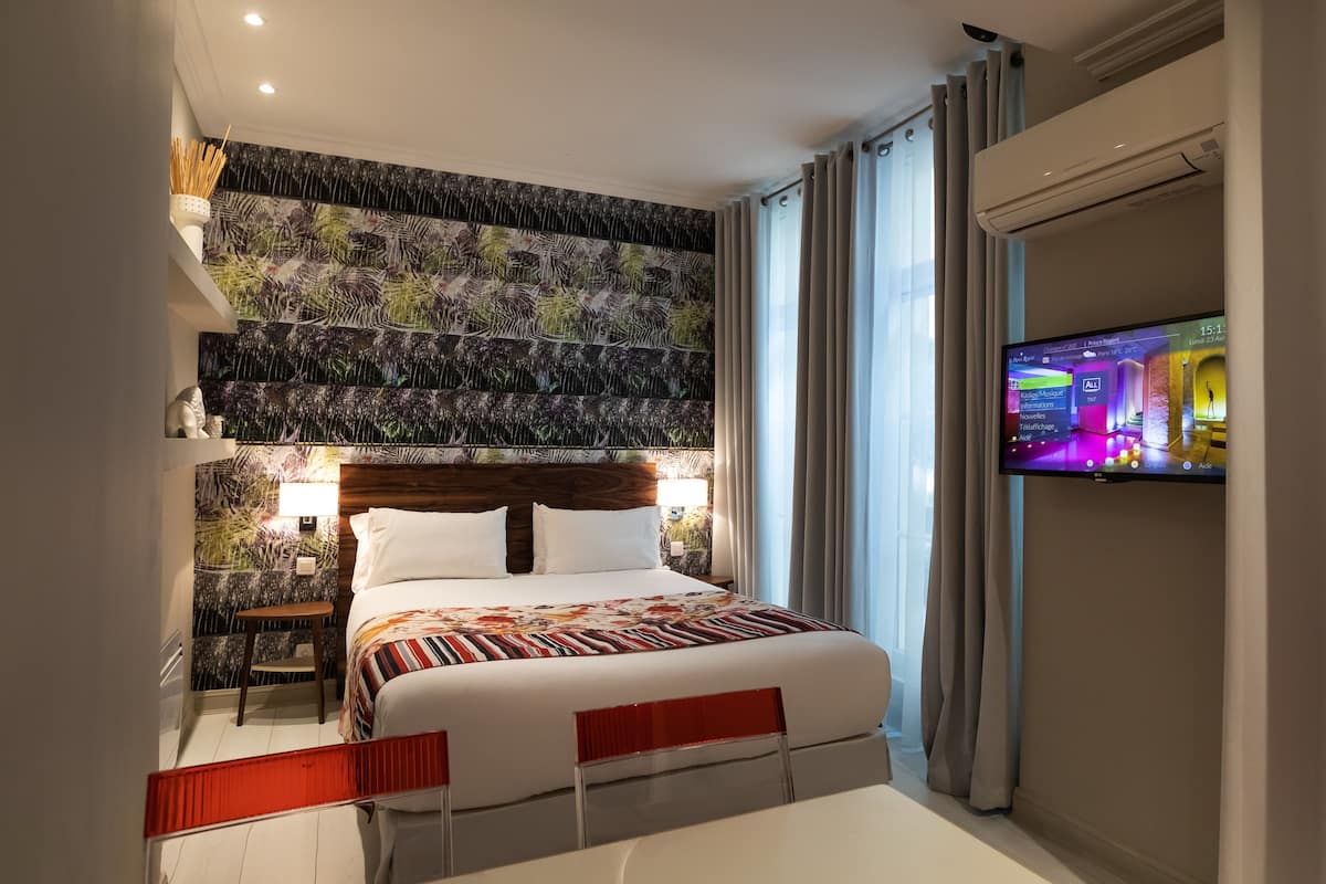 A modern hotel room with a large bed, a TV mounted on the wall, and a decorative wall panel.
