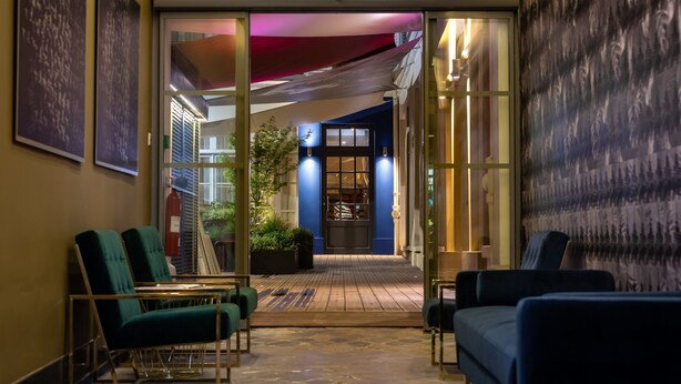 A hotel lobby with a wooden floor, green and blue seating, a fire extinguisher, and a blue door leading to the reception area. - Residence & Spa Le Prince Regent (Paris)