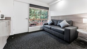 A modern room with a black leather sofa, a white door, a window with a view of greenery, and a microwave on a counter. - Bay City Motel Geelong (Geelong)