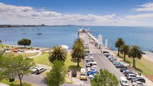 A coastal road with parked cars, palm trees, and a view of the sea with boats. - Bay City Motel Geelong (Geelong)
