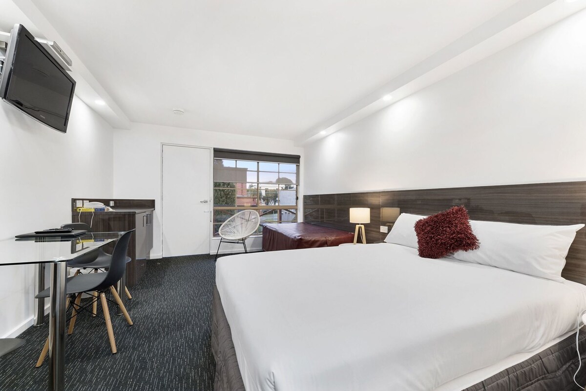 A hotel room with a bed, desk, chair, and a television.