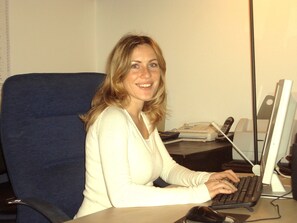 A person seated at a desk with a computer, a telephone, and a book. - Casa Giuditta Appartamenti (Palermo)