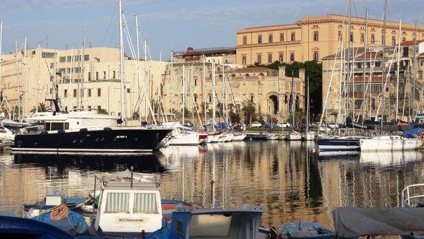 A marina with multiple boats docked, a historic building in the background, and calm water reflecting the boats. - Casa Giuditta Appartamenti (Palermo)