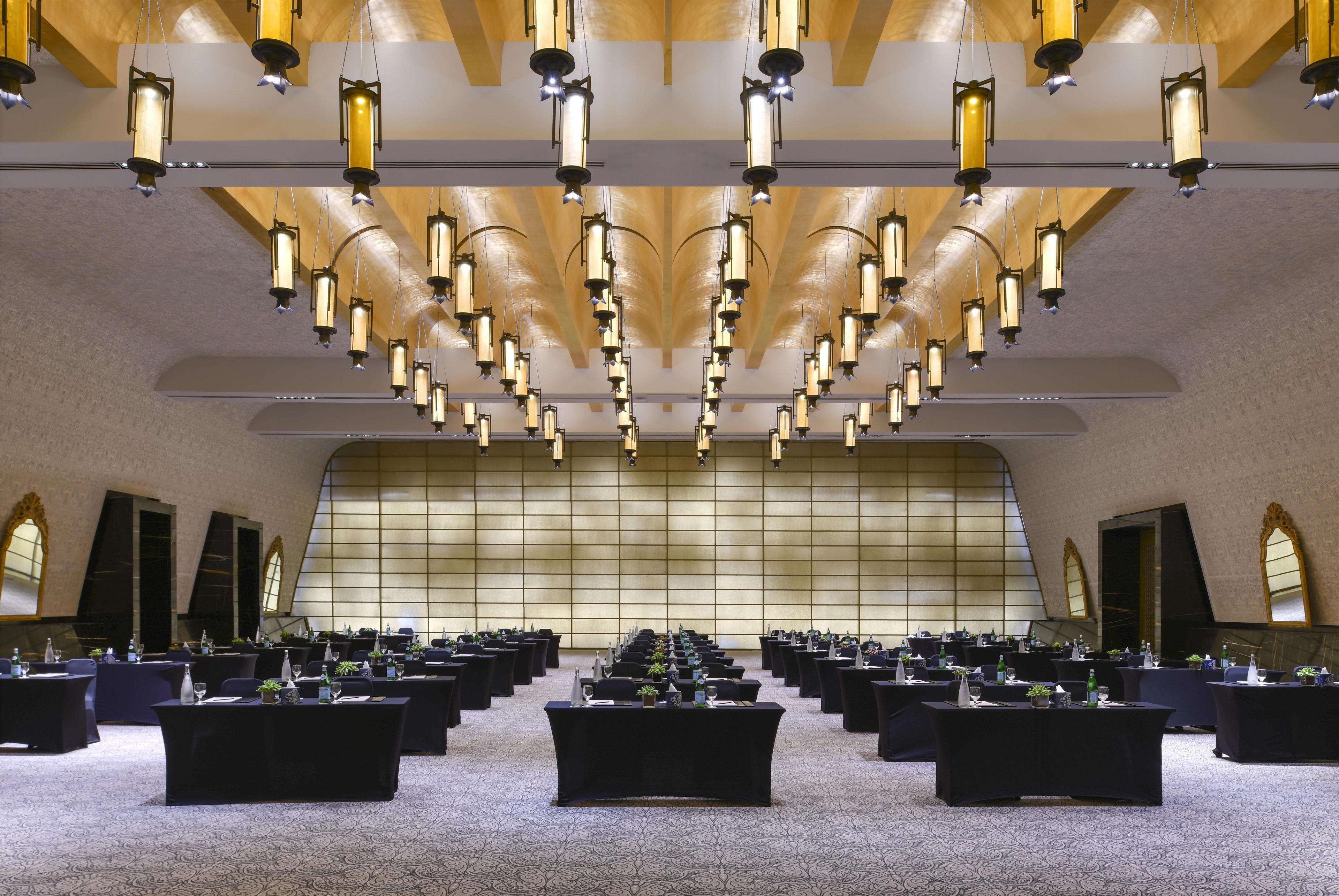 Un salón de conferencias con varias mesas, sillas y un techo alto con luces colgantes.