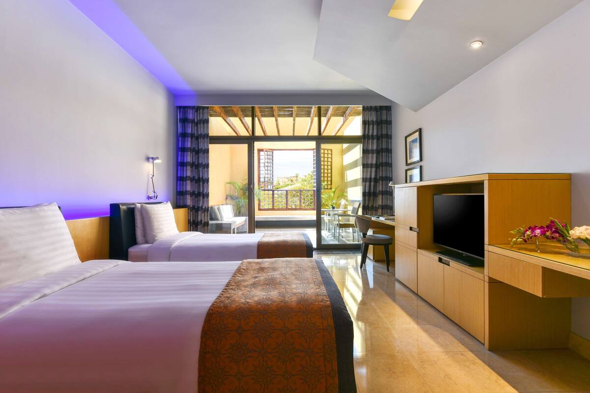 A hotel room with two beds, a TV, a desk, and a balcony with a view.
