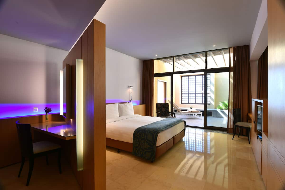 A modern hotel room with a bed, desk, chair, and large windows.