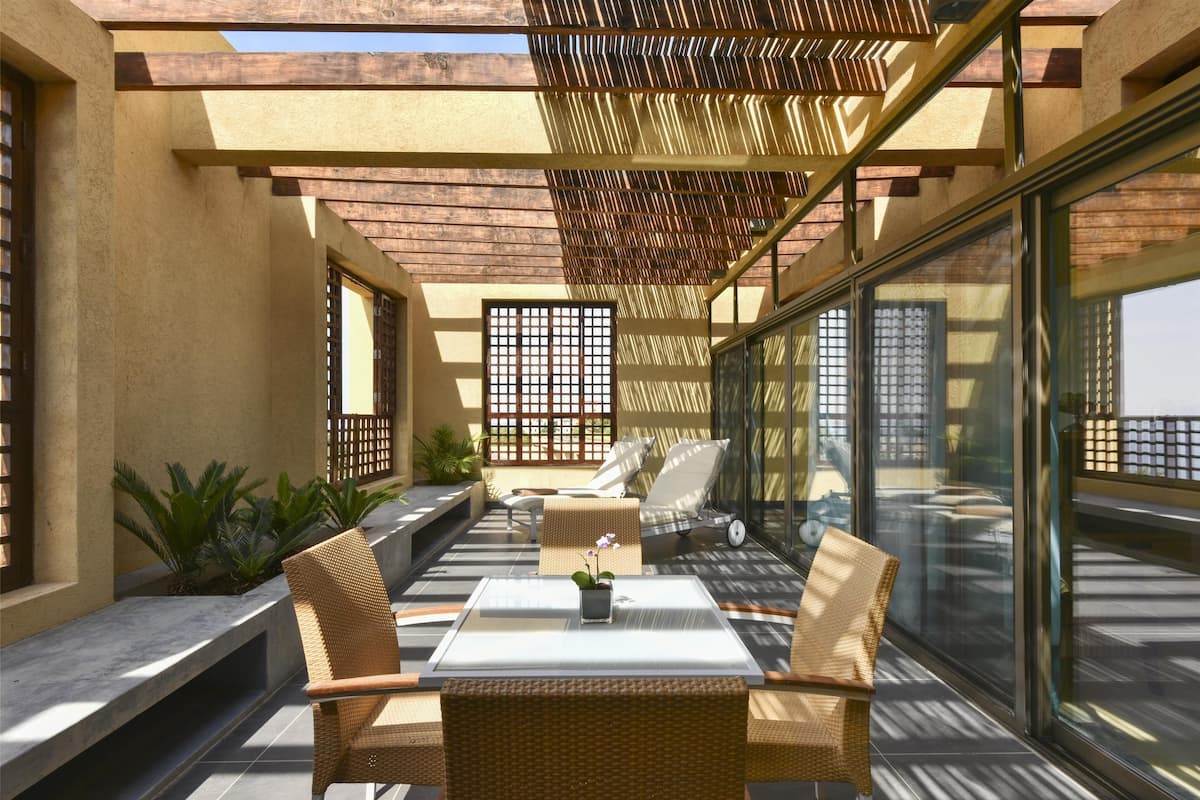 An outdoor patio with wicker furniture, a glass table, and potted plants.