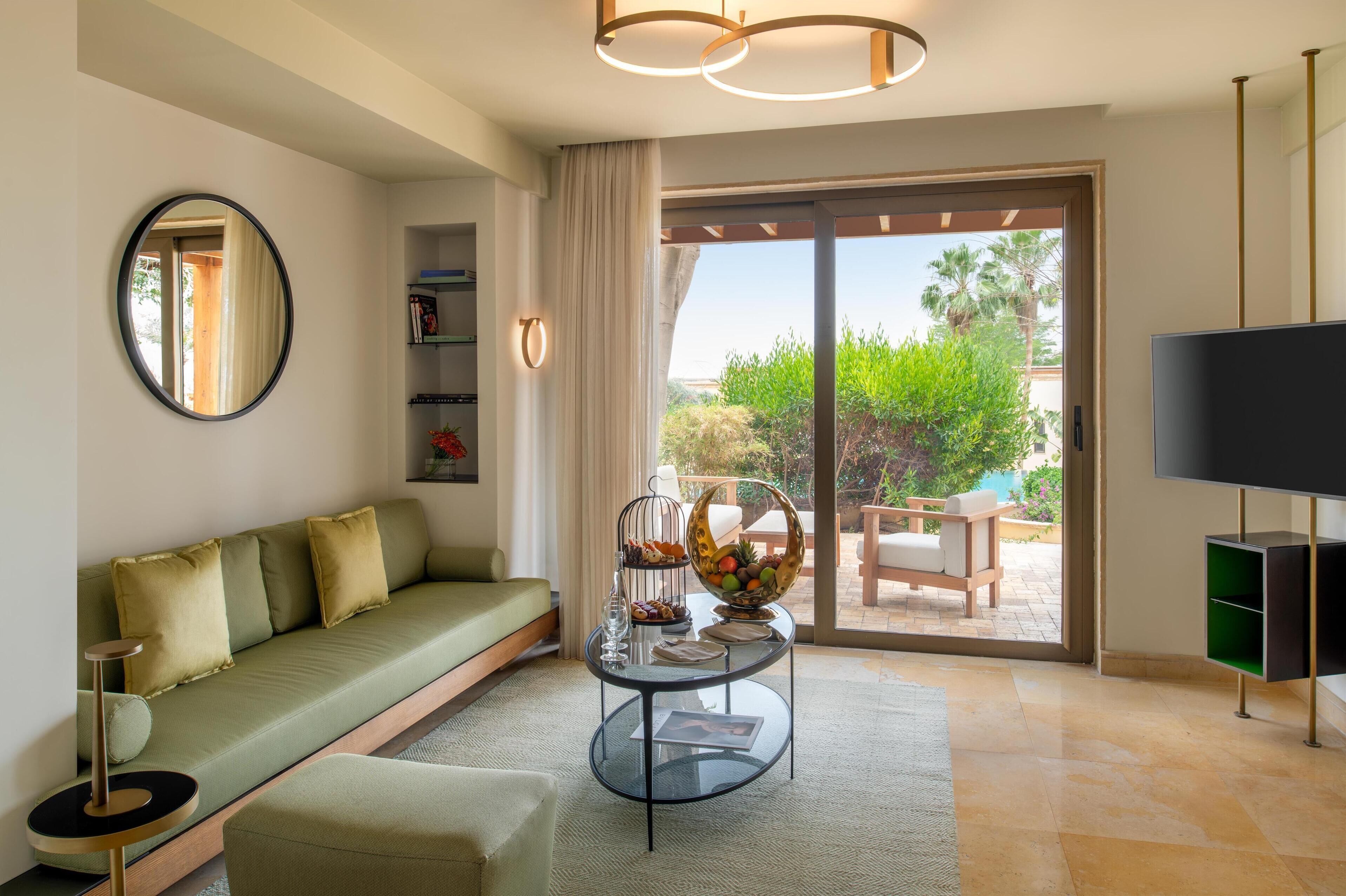 A modern living room with a sofa, a coffee table with fruit, a TV, and a view of the outdoors.