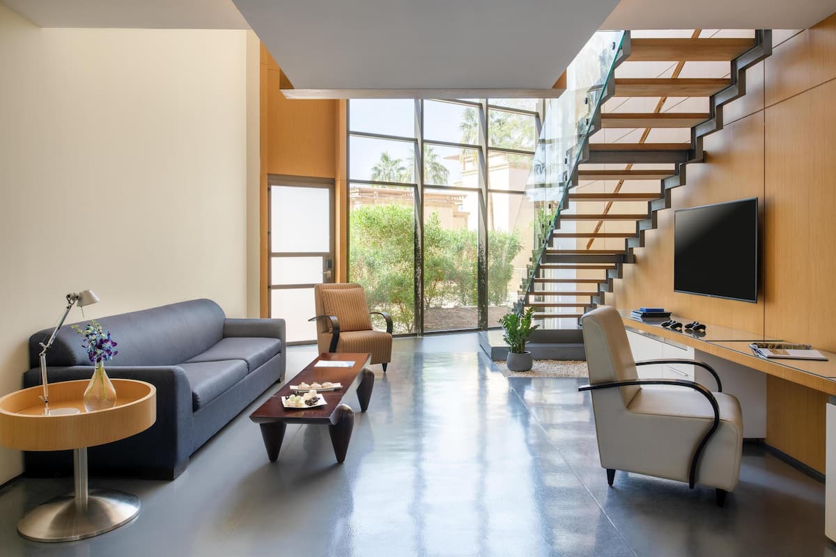 A modern living room with a sofa, coffee table, and chairs, a staircase, and a TV mounted on the wall.