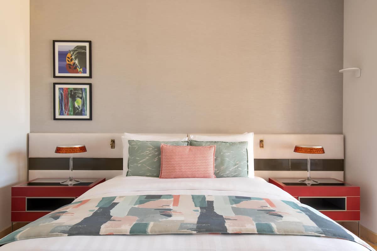 A neatly made bed with a colorful blanket, two bedside lamps, and two framed artworks on the wall.