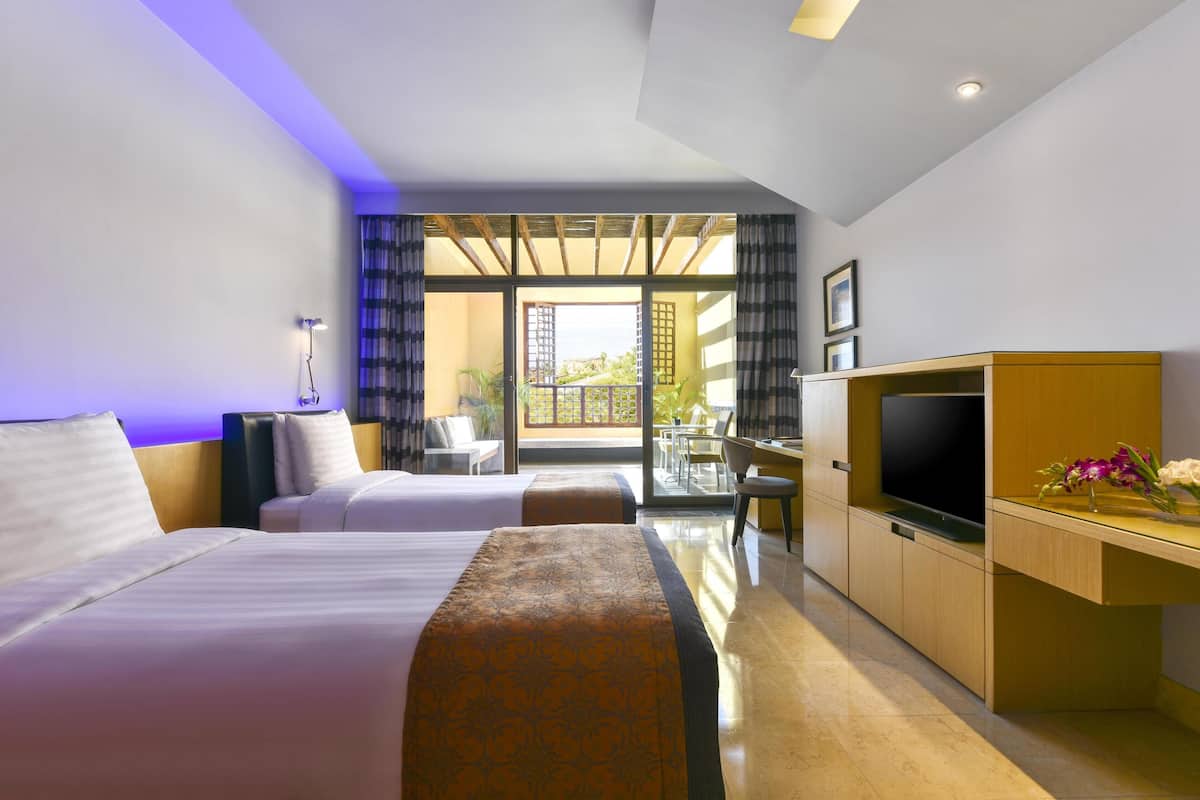A hotel room with two beds, a desk, a TV, and a balcony with a view.