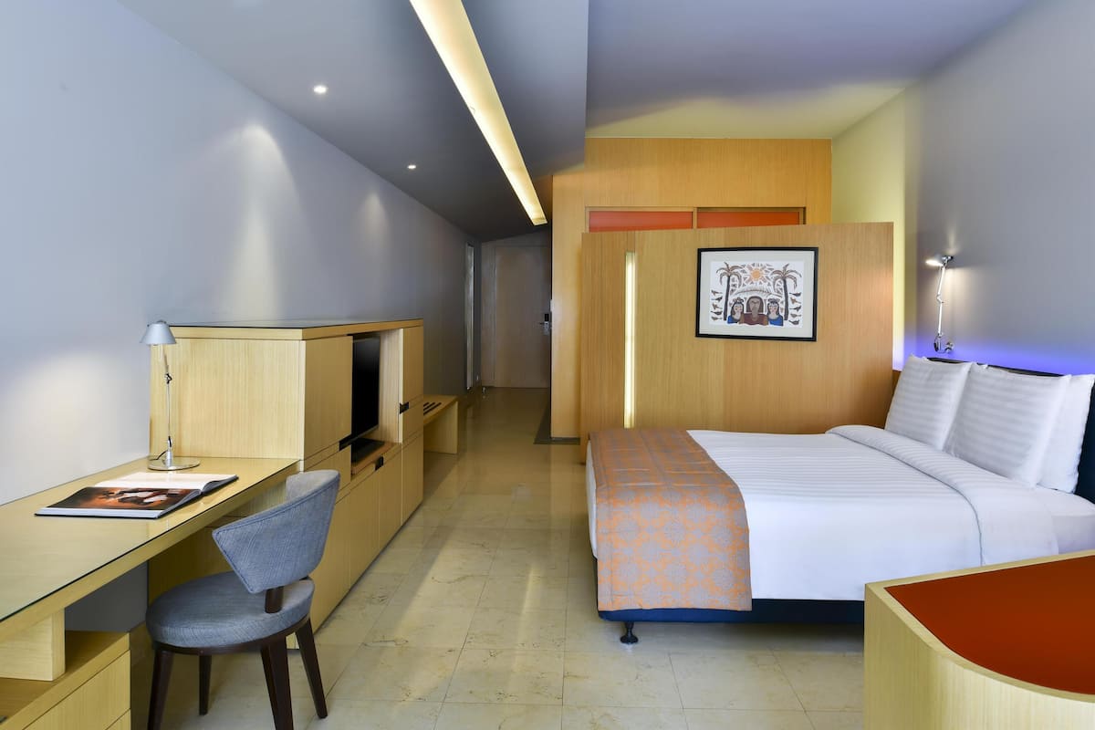 A hotel room with a bed, a desk, a chair, a TV, and a framed picture on the wall.