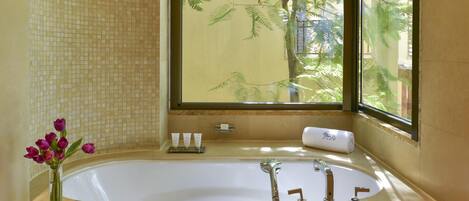 A bathroom with a large bathtub, a vase with flowers, and a window with a view of trees.