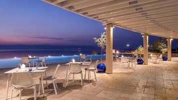 Un espace de restauration en plein air, avec des tables et des chaises, une pergola au-dessus et une vue sur la mer au crépuscule.