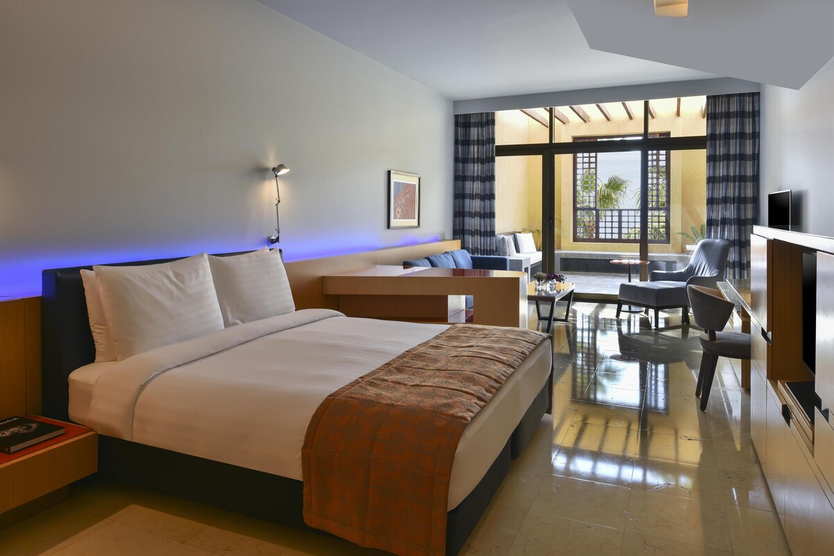 A hotel room with a large bed, a desk, a chair, and a TV.