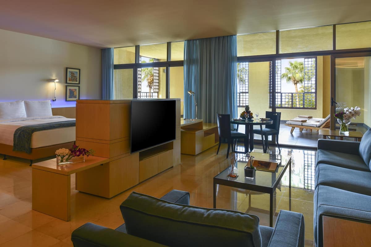 A modern hotel room with a bed, a TV, a sofa, a coffee table, and a dining area.