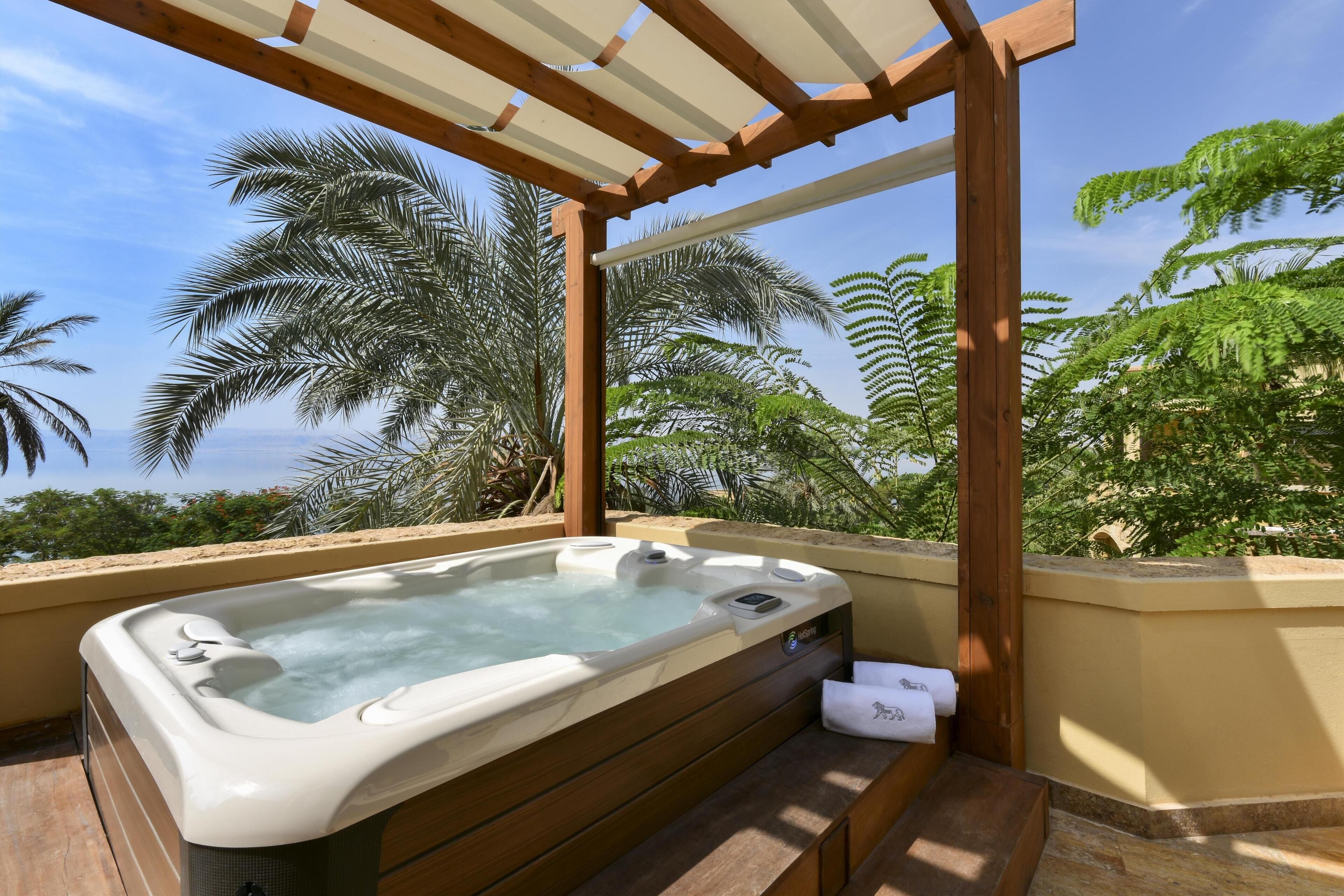 A hot tub under a wooden pergola with a view of palm trees and a clear sky.
