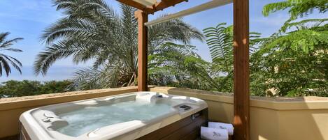 A hot tub under a wooden pergola with a view of palm trees and a clear sky.
