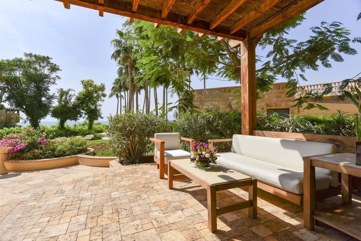 An outdoor patio area with a wooden pergola, a white sofa, and two wooden chairs.